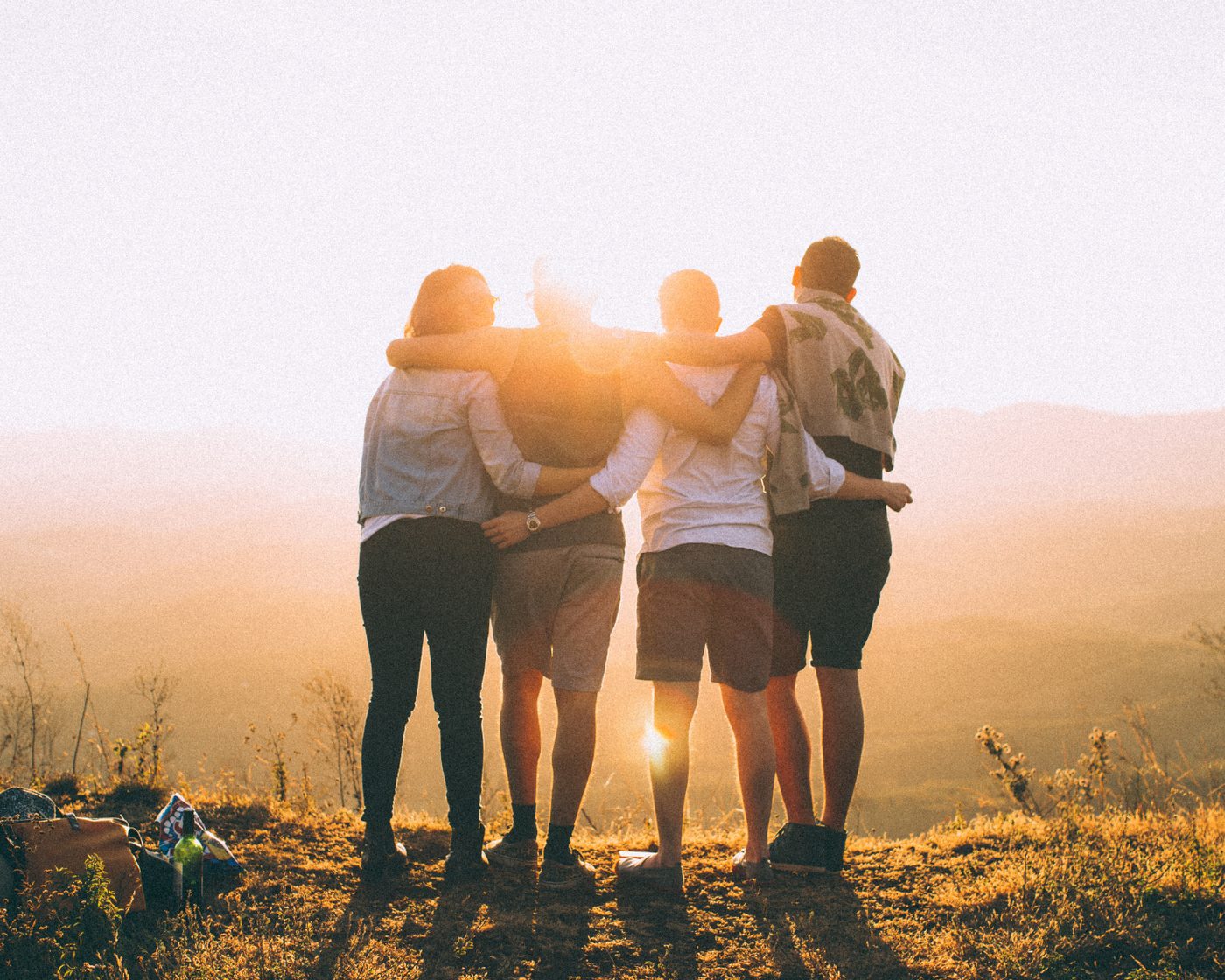 Four teens with arms around each other at sunset